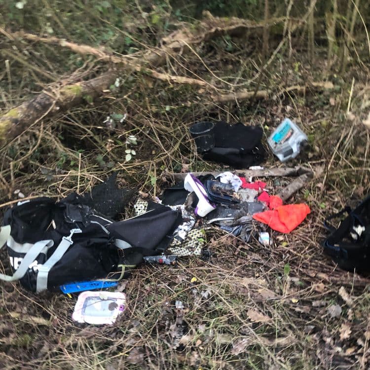 Liste des déchets abandonnés :

- Deux sacs à dos de sport noirs, approximativement 2 kg chacun (soit 4 kg au total).
- Un sac à main ou une sacoche noire, environ 1 kg.
- Une paire de chaussures de sport, environ 1 kg.
- Des vêtements divers : un vêtement rouge et un tissu à motif, probablement 0,5 kg au total.
- Un emballage de produit (boîte ou flacon), environ 0,2 kg.
- Un objet ressemblant à un jouet ou une tablette électronique, environ 0,5 kg.
- Divers petits déchets (emballages, etc.), environ 0,3 kg au total.

Total estimé : environ 7,5 kg de déchets.  Notez que ces estimations de poids sont approximatives et basées sur l'apparence visuelle des déchets dans l'image.
