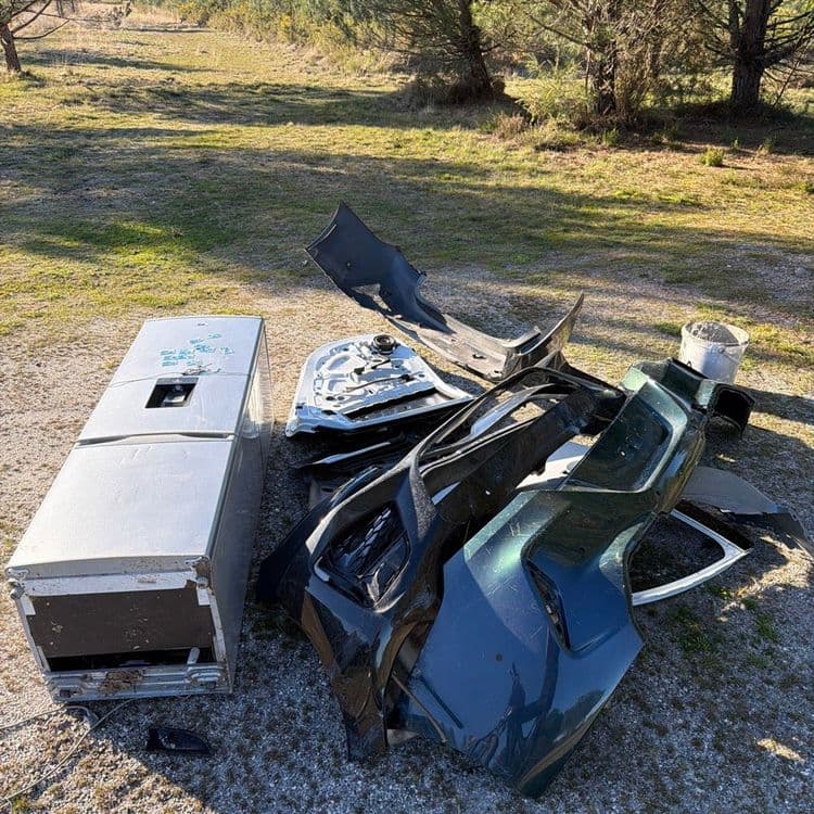 Suite à l'analyse de l'image, nous avons identifié les types de déchets suivants :

*   Un réfrigérateur (environ 60 kg) : Un appareil complet semble avoir été abandonné.

*   Éléments de carrosserie automobile (environ 40 kg) : On observe plusieurs pièces telles que pare-chocs, portière, et autres éléments de fixation. La quantité est d'environ 5 pièces.

*   Un seau en plastique (environ 2 kg) : Un seau est présent sur la zone, vraisemblablement en plastique.
