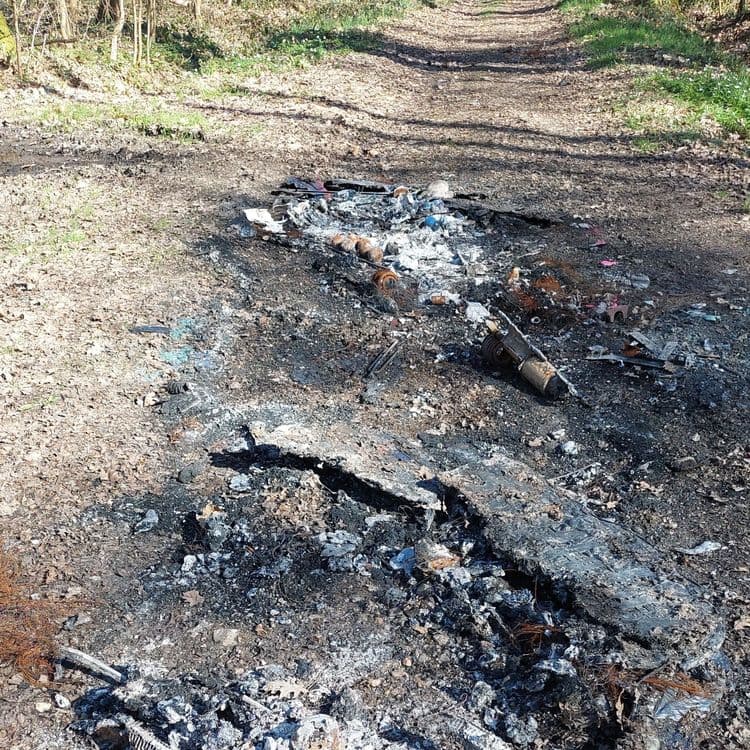 Voici une estimation des déchets présents sur le site, basée sur l'image fournie :

*   **Déchets incinérés divers** : Il s'agit d'un ensemble de résidus calcinés comprenant du plastique fondu, des restes de carton brûlé, des fragments métalliques rouillés (probablement ferreux), des textiles carbonisés et des cendres. Le poids total de ces déchets est estimé à environ 5 kg.
*   **Pneus** : Des restes de pneus partiellement brûlés sont visibles. On peut estimer qu'il y a environ 2 pneus en équivalent. Le poids total est d'environ 6 kg.
*   **Déchets métalliques** : Des éléments métalliques non identifiés sont présents, peut-être des pièces automobiles ou des objets divers. On peut estimer qu'il y a 1kg de déchets métallique.
*   **Déchets plastiques** : Des fragments de plastique non brûlés (ballon de baudruche) sont disséminés autour de la zone. On peut estimer 0.1kg de déchets plastique.
*   **Matelas** : Des restes d'un matelas partiellement incinéré sont visibles. On peut estimer qu'il y a 1 matelas en équivalent. Le poids total est d'environ 1 kg.
