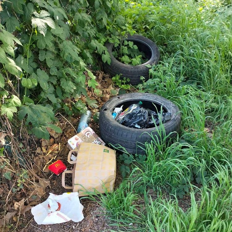 Deux pneus usagés et déchets divers abandonnés au bout d'une rue et à proximité d'un canal, en zone industrielle 