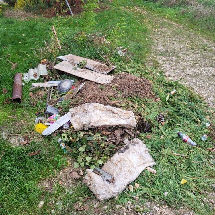 Voici une estimation des déchets présents sur l'image :

*   **Isolant (laine de verre ou similaire) :** Environ 5 kg, en deux gros morceaux.
*   **Bois (planches) :** Environ 3 kg, en deux planches.
*   **Fibrociment (plaque ondulée) :** Environ 2 kg, un fragment.
*   **Métal (tube, récipient) :** Environ 1 kg, divers éléments.
*   **Déchets verts (branchages de conifères, feuilles) :** Environ 4 kg.
*   **Divers (plastique, emballages, canettes) :** Environ 1 kg, en plusieurs unités.
