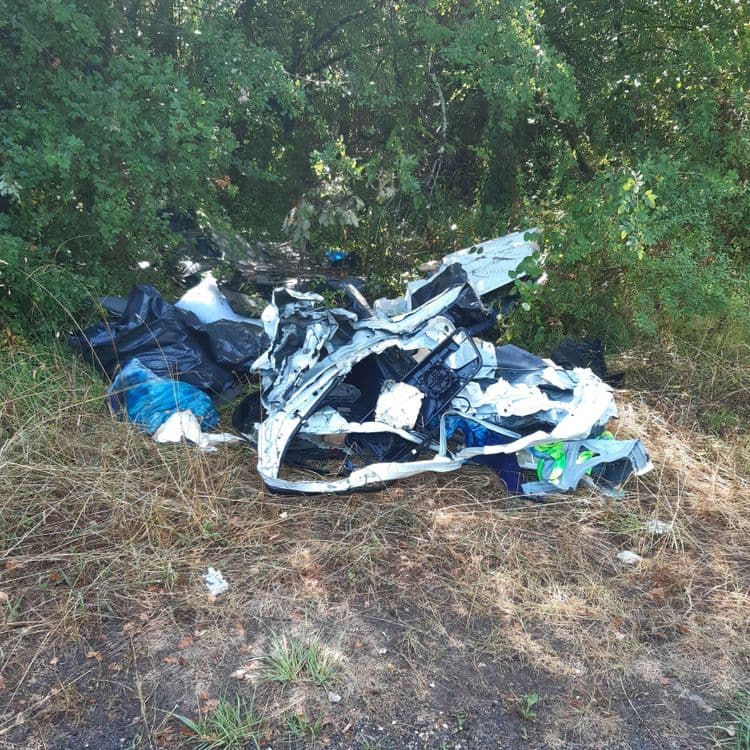 Suite à l'examen de l'image, les déchets suivants ont été identifiés :
* **Débris de véhicule** : Incluent des éléments de carrosserie (pare-chocs, éléments de structure), des pièces en plastique (tableaux de bord, garnitures), et potentiellement des composants mécaniques. Le poids total est estimé à environ 50-70 kg, compte tenu de la quantité et de la densité des matériaux.
* **Sacs poubelles** : Contiennent un mélange de déchets ménagers divers (emballages, déchets organiques, etc.). Il y a environ 2 sacs visibles, avec un poids estimé de 5-10 kg par sac, soit un total de 10-20 kg.
* **Déchets plastiques divers** : Composés de fragments de plastiques non identifiables (bouteilles, emballages, etc.). Le poids total est estimé à environ 5-10 kg.
* **Textiles** : La présence de textiles est suggérée (housse, tissus). Le poid total est estimé à environ 1-2 kg.